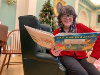 Stephanie Holman, children’s librarian, Belfast Free Library, enjoys one of the gardening books for kids donated by Belfast Garden Club. (Photo courtesy Belfast Garden Club)