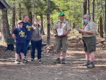 Drew Riddle of Randolph received his Wood Badge beads and certificate during the annual Pack and Troop 672 campfire. His son Webelos Cub Joshua, his wife Christina who is also the Webelos Leader for Pack 672, and his son 2nd Class Scout Connor look on after Karen Norton, the Wood Badge Course director, has finished the presentation. Norton is wearing the mask.