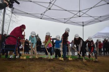Ceremonial gold shovels push the starting layer of dirt that will one day become the CTE/Makerspace building at St. George School. From left to right: Diana Bean, Ella Walvatne (3rd grade), Luna Waters (2nd grade), Gunnar Jeffers (PreK), Ben Lord (6th), Olivia Myers (8th), and Byron Marves (5th). (Photo by Sarah Thompson)