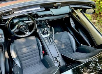 All we need and nothing more, including elbow room. Aft of the short-throw 6-speed gear lever is the computer control knob (the screen is hidden by the driver’s sun visor), the radio knob and a small storage compartment. In lieu of a glove box, there’s another small compartment between the seatbacks. The shiny rear slab of roof provides roll-over protection. The seats adjust manually but are heated. Note the electric window switches and mirror controls (unheard of in vintage roadsters) and, for those movie-stunt turns, the handbrake lever. Yes, an automatic transmission is available. If you insist.