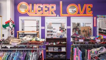a look inside a thrift store, with a sign reading queer love hanging on the wall.