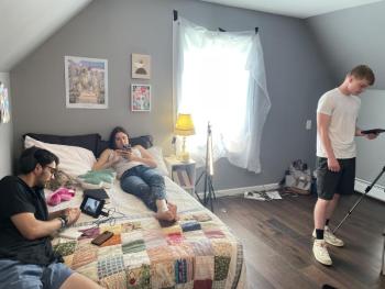 Director Michael Russillo, left, is preparing to shoot a scene of 'Rivers Edge' in Northport with Cora Maple Lindell (center) and Isaiah Morrissey (right). (Courtesy photo) a standing man operates a camera while another one looks at a camera monitor and a woman lays nearby looking at her cell phone.