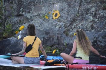 A sunflower helps identify a plaque for Sunshine Stewart that's mounted to a cliffside boulder on an island in Crawford Pond. (Photo by Sarah Thompson)