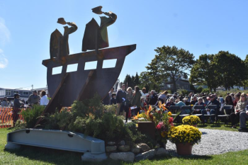 View of a memorial sculpture with ceremony attendees in the background.
