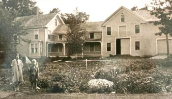 Large old house with garden in foreground and two children posing to the side for the picture