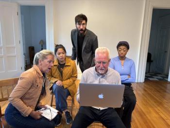 Four people look at a laptop with various expressions on their faces