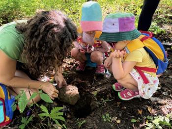 Woman and two toddlers squat down to peer into a hole