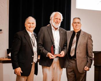 Three men. Man in middle holds award.