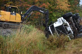 An excavator pushes gravel away from the bed of a dump truck