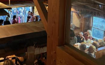Inside Flatbread Pizza, Graham Platner positions himself at the door so that he can speak to the crowd inside the restaurant and the crowd outside the restaurant. 