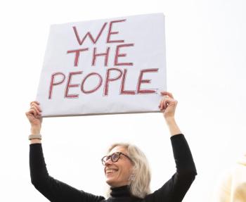 Female protestor holds a sign "We the People"