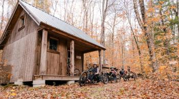 Four people ride adaptive mountain bikes toward a structure