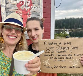 Selfie picture of two women holding a cup of chowder and a sign