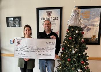 Woman and man hold oversized check next to Christmas tree