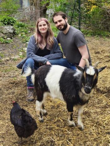 woman and man squat for photo with goat and chicken