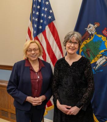two women pose in front of state, federal flags
