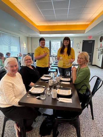 Students wearing yellow shirts serve a group of women