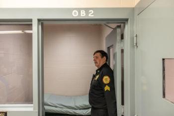 A corrections officer stands to the side in a doorway. 