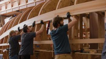 three men place board for a ship's hull
