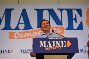 Troy Jackson stands behind a podium, smiling.