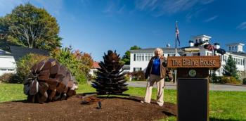 woman, lectern, two pine cone sculptures