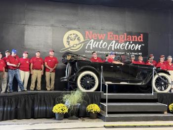 people in red shirts stand behind car on auction block 
