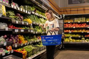 a woman places a vegetable into her shopping basket. 