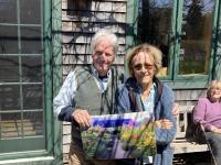 Barbara and Elliot are holding a painting of the garden in high season.