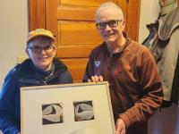 Rotarian Peter Lindquist (right) presents a dyptych pastel by the late Paul Plante to lucky winner Ali Dailey.