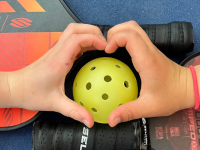 Hands shaped into hearts over a pickleball and paddles