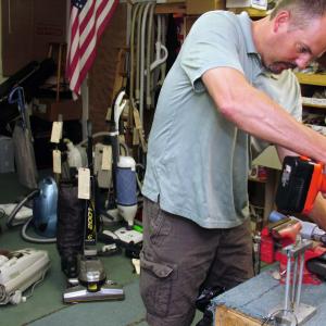 Jeff's Vacuum proprietor Jeff Hall works on a broken vacuum cleaner swivel head — a common repair — in the back room of his shop in West Rockport. (Photo by Ethan Andrews)