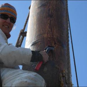 Capt. Brenda Thomas scraping the mast of Schooner Isaac H. Evans