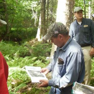 Lands committee members look on as Jim R. Robbins reviews a map of the property, with Jim A. Robbins in the background. (Photo courtesy of Georges River Land Trust)