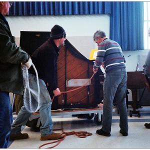 BELFAST - A piano donated by Bruce Starret arrives at Belfast Area High School. Music teacher John Cameron, striped shirt, said new instrument will allow for piano duet recitals without moving a third piano off the auditorium stage each time. (Photo by Ethan Andrews)