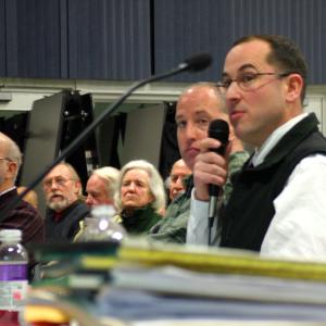 Mike Lucy, with microphone, and Frank Gallagher, behind Lucy, of the security risk consulting firm Good Harbor, detail their company's report to the Searsport Planning Board and roughly 200 people in attendance at a public hearing on Monday night (Photo by Ethan Andrews)