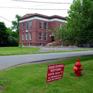 A sign put out by supporters of a six-town movement to withdraw from the consolidated Regional School Unit 20 stands outside the former Peirce Elementary School in Belfast, a casualty of a previous consolidation. Municipalities around the state go to the polls on June 11 to validate local school district budgets. Some will have additional questions to reckon with. (Photo by Ethan Andrews)
