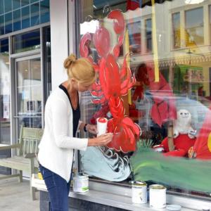 Marjanne Raddmaker of Owls Head paints the windows of Planet Toys for the Lobster Festival that begins Wednesday. (Photo by Ron Hawkes)
