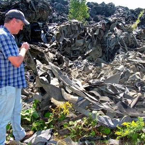 Michael Parker of the Maine Department of Environmental Protection lifts some of the synthetic upholstery stockpiled on the property of a defunct shooting range in Warren. DEP is seeking proposals for reusing the material, which currently poses a fire hazard. (Photo by Ethan Andrews)