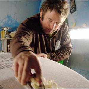 Monroe Surf Co. owner Josh Moody shaves the wooden “stringer” support embedded in the foam “blank” that will eventually become a custom-designed surfboard. For this photo, Moody removed the respirator that he normally wears in the shop. (Photo by Ethan Andrews)
