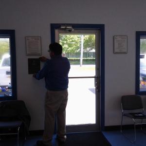 Photo: Brad Overlock hangs the Better Business Bureau certificate in their new space. (Photo by Jessica Fossett)