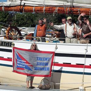 Capt. Doug Lee, in suspenders, and guests aboard his schooner, Heritage, wave as they finish tying up at the Camden Town Dock. Meg Sharp, the Camden Windjammer Festival official greeter, is on the dock, having delivered a welcome pineapple to Lee. (Photo by Holly S. Edwards)