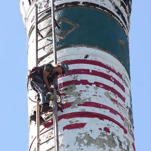 Dustin Frazier, of Gibraltar Chimney International, pulls up a lag bolt drill on a rope while attaching 170-feet of ladder to the exterior of the Knox Mill smokestack Tuesday morning. (Photo by Holly S. Edwards)