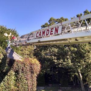 Camden firefighter Cheyne Hansen places the Camden Public Library’s gold rooster back atop its weathervane perch on one of two gatehouses at the entrance to the Amphitheatre. (Courtesy Camden Fire Department)