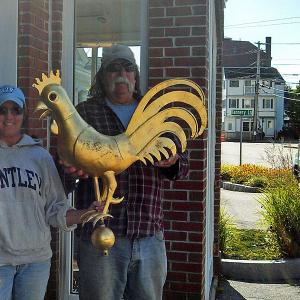 Camden Parks and Recreation crew members Richelle Gagne and John Gould pose with the gold-leaf rooster that was left in the bed of their work truck earlier in the morning Sept. 10. The rooster, which tops one of two weathervanes on the gatehouses at the entrance to the Camden Public Library Amphitheatre, was reported stolen Monday morning. (Courtesy Camden Police Dept.)
