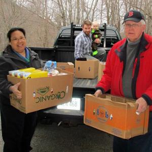 From left, Rockport Select Board members Tracy Murphy and Owen Casas (holding his son), help unload donated food with Camden Select Board member Don White.
