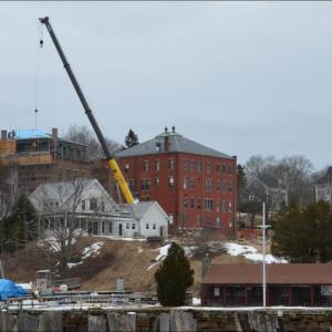 Looking north over Rockport Harbor in 2013 to the Shepherd Block, the large brick structure near Union Hall (which the crane operator is working on). The two buildings have undergone extensive renovations over the past decade by Leucadia Corp. and its subsidiary LLCs in the Midcoast since 2005. Now, a local family that invests in real estate plans to purchase it and keep it in commercial use. (Photo by Lynda Clancy)