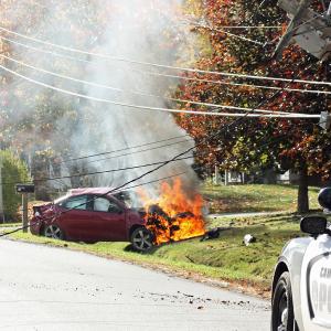 It did not take long for the fire inside the engine compartment of Kevin Curit’s 2014 Dodge Dart to burn in earnest Monday afternoon, after he went off the road, became airborne, shattered a utility pole, possibly rolled in midair, and came to rest facing the wrong way from where he came. (Photo by Holly S. Edwards)