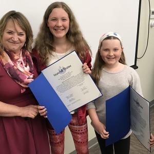 From left, Dorothy Havey, special assistant to Senate President Michael Thibodeau, with Isabella and Maren Kinney during Monday night’s Lincolnville Board of Selectmen’s meeting, at which the Kinney sisters were honored with a Legislative Sentiment and learned that the 2017 Town Report had been dedicated to them for their role in saving a life – their father, Town Administrator David Kinney. (Photo by Holly S. Edwards)