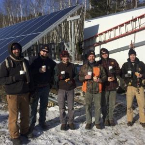 Below, the ReVision Energy Camden installation team warm up upon completion of Camden’s solar array in frigid temperatures. From left to right: Ren Floyd, Jerod Elder, Arthur Nerzig, Andy Lesko, Justin Milliken, and Hans (and Turner) Albee. (Photo courtesy Jennifer Albee)