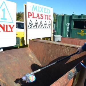 Beth Kwiatkowski mans the front desk at the Midcoast Solid Waste Transfer Station in Rockport, and holds up a No. 1 plastic container. This plastic will get baled and shipped to southern Maine to enter the recycling market. (File photo by Lynda Clancy)
